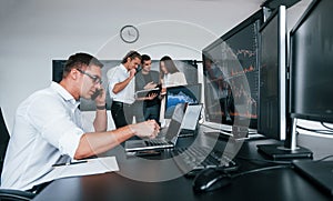 Man uses laptop. Team of stockbrokers works in modern office with many display screens