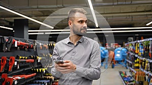 A man uses a phone by choosing goods in hardware store