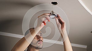 A man uses pliers while repairing a ceiling LED light fixture