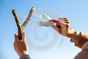 Man uses a protective medical mask as a slingshot from tree branch, blue sky on background, Quarantine is over