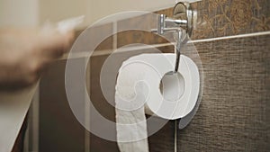 A man uses a roll of toilet paper. Unwinds it.