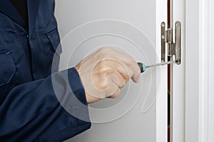 man uses a screwdriver to screw the hinge of a door