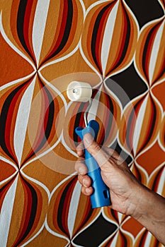 man uses a seam roller on a wallpapered wall