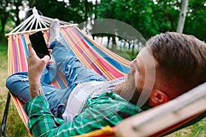 Man using an app on his mobile phone white swinging in a hammock.