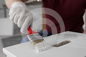 Man using brush to paint bekvam with white dye indoors, closeup