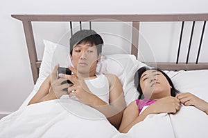 Man using cell phone while looking at woman sleeping in bed