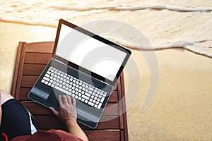 A man using computer laptop on wooden sunbath lounge chair on the beach in summer at sunset. Clipping path computer notebook scree