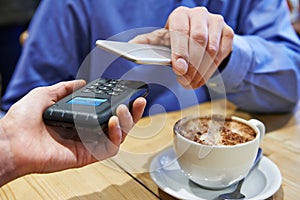 Man Using Contactless Payment App On Mobile Phone In Cafe