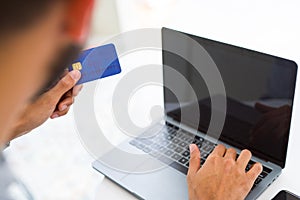 Man using credit card as payment metod when shopping online using laptop, blank screen concept