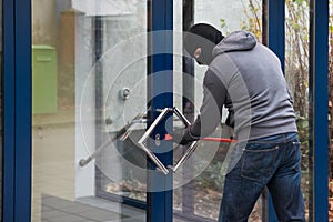 Man Using Crowbar To Open Glass Door