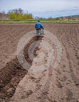 Man using a cultivator in a field on a farm, before planting potatoes