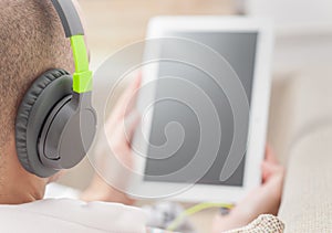 Man using digital tablet computer at home wearing headphones