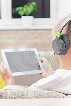 Man using digital tablet computer at home wearing headphones