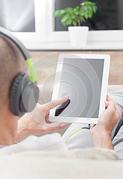 Man using digital tablet computer at home wearing headphones