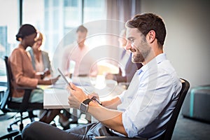 Man using digital tablet while coworker interacting in the background