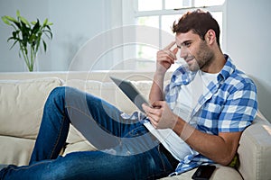 Man using digital tablet while relaxing on sofa