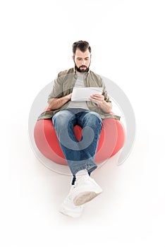man using digital tablet while sitting on bean bag chair,