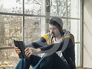 Man using a digital tablet while sitting on the windowsill