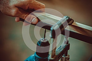 Man using the drill makes a hole in wood and iron strap.