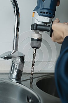 man using a drill to make a hole in a kitchen sink