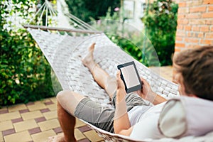 Man using e-book or tablet computer while relaxing in a hammock