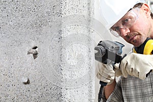 Man using an electric pneumatic drill making a hole in wall, professional construction worker with safety hard hat, hearing