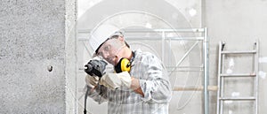 Man using an electric pneumatic drill making a hole in wall, professional construction worker with safety hard hat, hearing