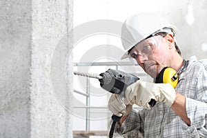 Man using an electric pneumatic drill making a hole in wall, professional construction worker with safety hard hat, hearing