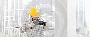 Man using an electric pneumatic drill making a hole in wall, professional construction worker with safety yellow hard hat, hearing