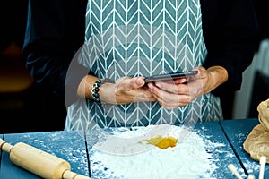 Man using electronic tablet pc in kitchen at home for baking. Man searching for food recipe in tablet computer.