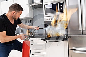 Man Using Fire Extinguisher To Put Out Fire From Oven