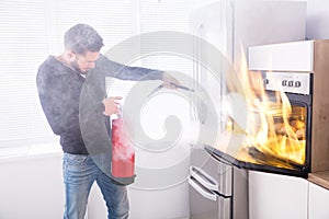 Man Using Fire Extinguisher To Stop Fire Coming From Oven