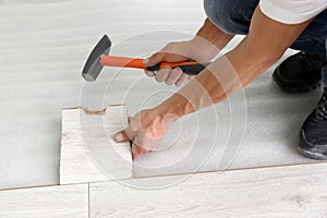 Man using hammer during installation of new laminate flooring, closeup