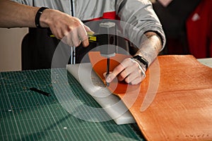 A man using a hammer and a punch makes holes for hand-stitching a leather product