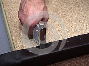Man using hand-tool stapler and leatherette upholstering particle board