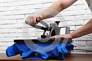 Man using heat press machine at table near brick wall, closeup