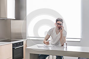 Man using his cell phone while working on finances in his home kitchen