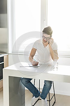Man using his cell phone while working on finances in his home kitchen