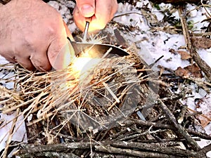 Man using his knife and fire starter to get fire going. Winter camping.