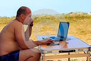 Man using his laptop sitting at a folding picnic table in a camping. Working while traveling. Freelance work. Work and travel