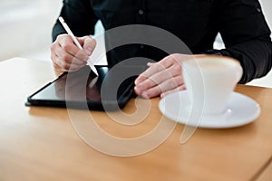 Man using his tablet with stylus. opy space screen on gadget. Cut close up view of man in black clothes sitting with cup of coffee