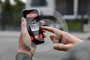 Man using home security application on smartphone in front of house outdoors, closeup