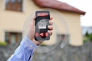 Man using home security application on smartphone in front of house outdoors, closeup