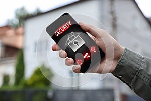 Man using home security application on smartphone in front of house outdoors, closeup