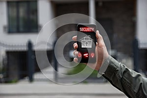 Man using home security application on smartphone in front of house outdoors, closeup