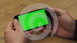 Man using horizontal smartphone with green screen. Close-up shot of man`s hands with mobile phone. Chroma key. Close up