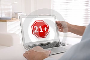 Man using laptop with age limit sign 21+ years indoors, closeup