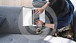 Man using laptop computer while sitting with his cat on comfortable couch.