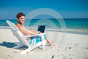 Man using laptop on deck chair at the beach