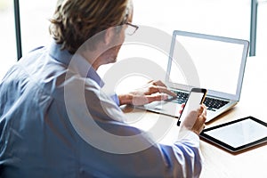 Man using laptop while holding phone in office